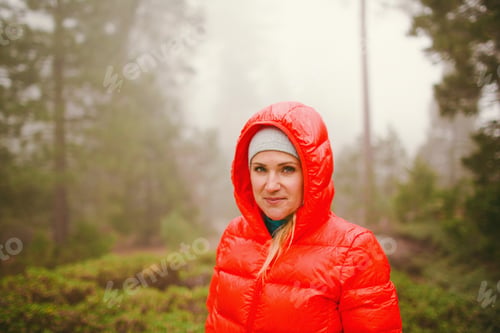 Preview: Woman in a red jacket standing in a misty forest.
