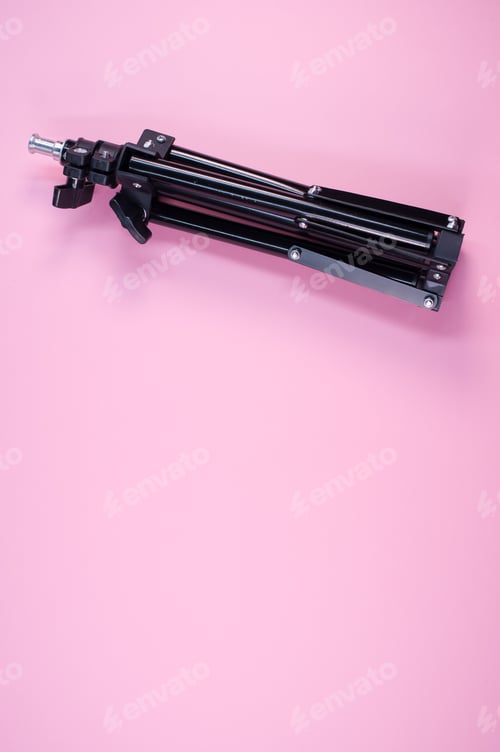 Preview: Closeup shot of a black iron folding tripod on a pink background with a copy space