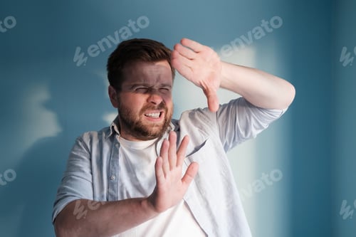 Preview: European man is annoyed by the sunlight, which blinds him. Blue background.