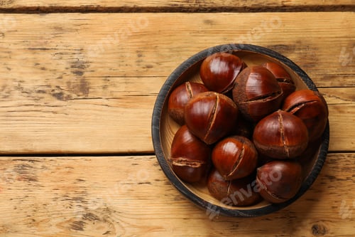 Preview: Fresh edible sweet chestnuts in bowl on wooden table, top view. Space for text