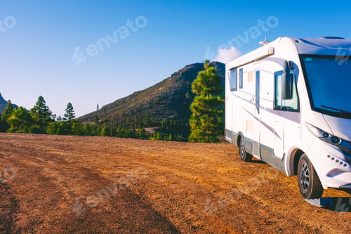 Preview: White motorhome parked on a mountain overlook with clear blue sky and pine forest view