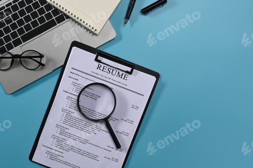 Preview: Top view laptop computer, magnifying glass and resumes applicants on blue background.