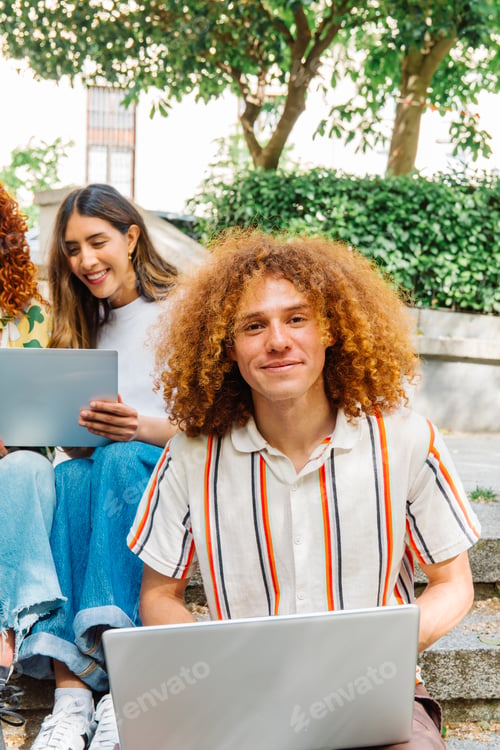 Preview: College student using a laptop, sitting with his classmates on the steps of the campus garden
