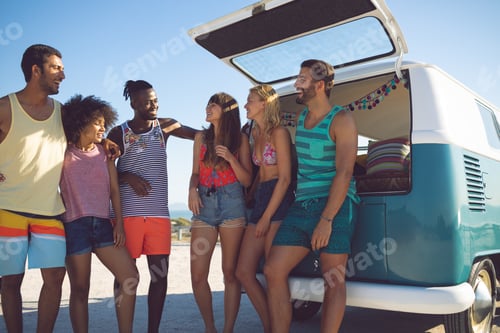 Preview: Front view of happy group of diverse friends interacting with each other near camper van at beach
