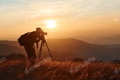 Preview: Male photographer standing and working at majestic landscape of autumn trees and mountains