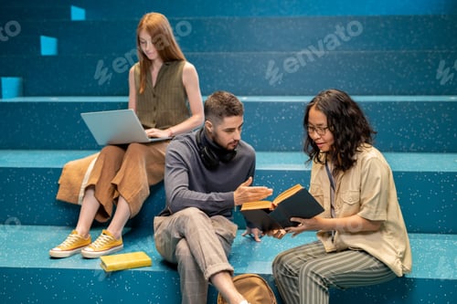 Preview: Confident student explaining something to female groupmate while pointing at page of book