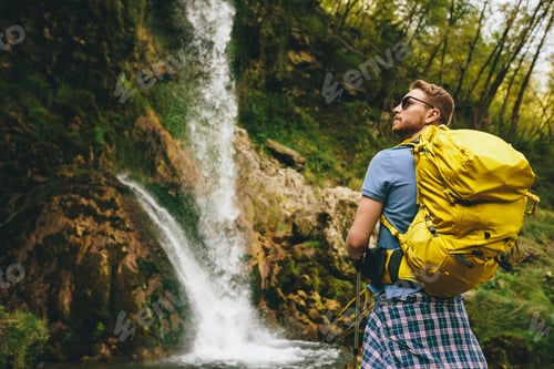 Preview: Young hiker stopped beside a mountain waterfall to rest
