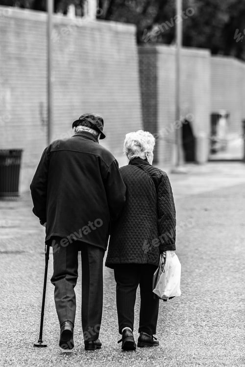 Preview: Vertical greyscale shot of an old romantic couple walking holding hands