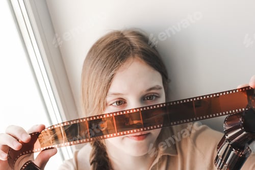 Preview: Old vintage retro film negative for camera in the hands of cute teenage girl looking on it. N