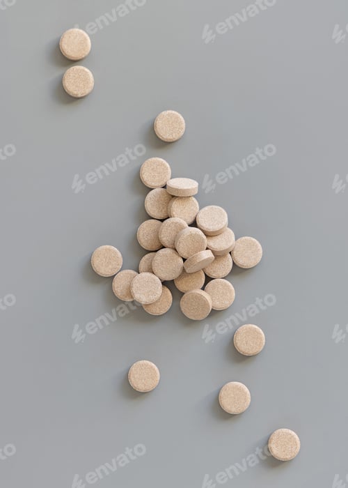 Preview: Pile of beige herbal pills on grey top view. Taking dietary supplements and vitamin