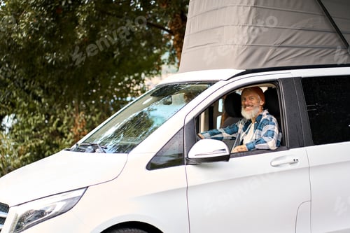 Preview: Happy older man traveler driving camper van sitting inside, campervan rentals.