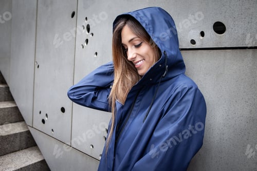 Preview: A millennial girl dressed in a blue raincoat wet from the rain smiles.