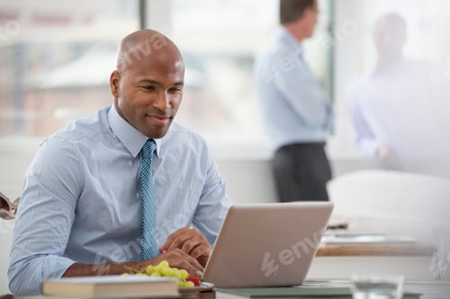 Preview: A business environment. A businessman in a shirt and tie sitting at a desk, using a laptop computer.