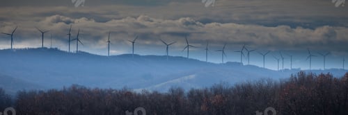 Preview: Panoramic shot of wind turbines on a mountain top against a cloudy blue sky