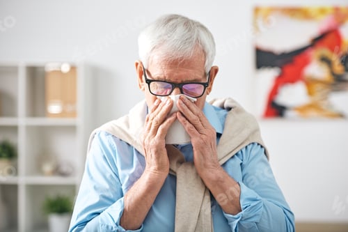 Preview: Sick senior retired man with handkerchief by his nose staying at home