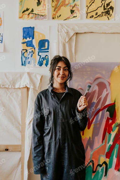 Preview: Woman artist holding a paint brush in front of her artworks