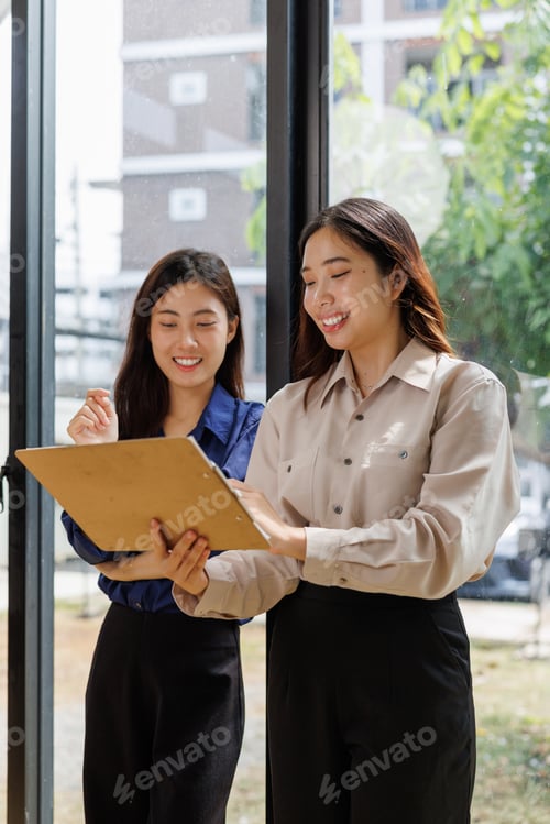 Preview: Asian businesswomen collaborating, reviewing documents on clipboard