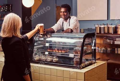 Preview: African American barista in uniform giving a cup of coffee to his client at the trendy coffee shop