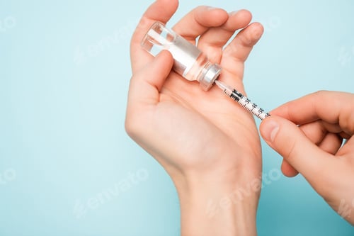 Preview: Cropped view of man with syringe picking up hormonal drug from jar on blue surface