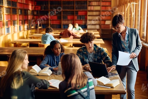 Preview: High school teacher using laptop with her students in a library.