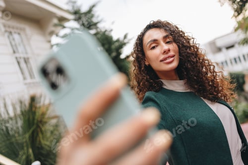 Preview: Young brunette woman with curly hair taking a photo over street