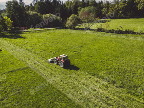 Preview: Aerial view of a red tractor mowing a green grass field on a sunny spring day