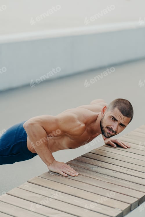 Preview: Vertical shot of muscular bearded man stands in plank pose trains chest and arms muscles
