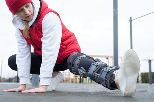 Preview: Woman wearing knee brace or orthosis after leg surgery working out in the park