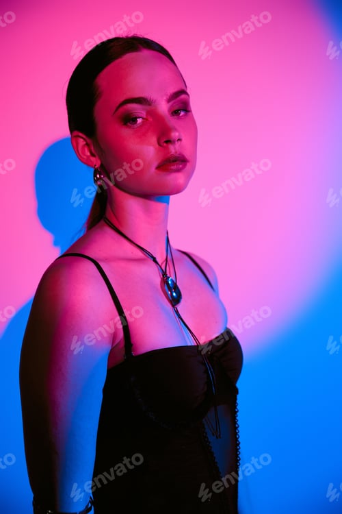 Preview: Stylish young woman posing in studio with vibrant pink and blue lighting