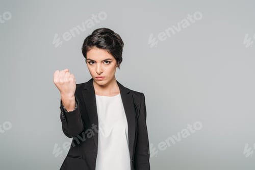 Preview: angry mixed race businesswoman looking at camera and showing fist isolated on grey