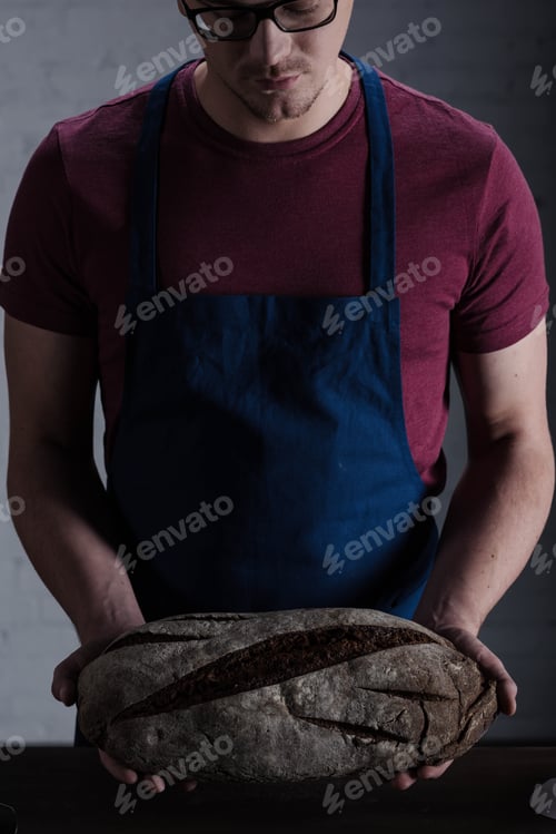 Preview: Male baker holding fresh baked bread loaf in hands