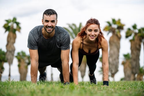 Preview: Joyful satisfied and athletic male and female sitting in the grass in sportswear training workout