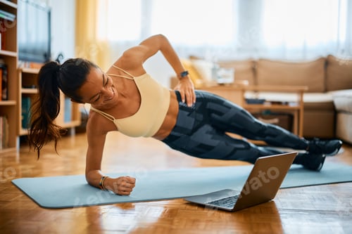 Preview: Happy woman in side plank pose having fun during online exercise class at home.