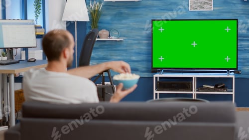 Preview: Man relaxing on couch looking at green screen on tv watching movie while eating popcorn