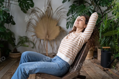 Preview: Dreamy woman relaxing in tropical resort-style garden at home, female gardener resting in greenhouse