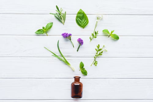 Preview: top view of bottle of natural herbal essential oil and scattered green leaves on white wooden