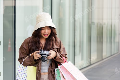 Preview: Young Asian woman enjoying shopping lifestyle, holding colorful fashion bags, using camera near