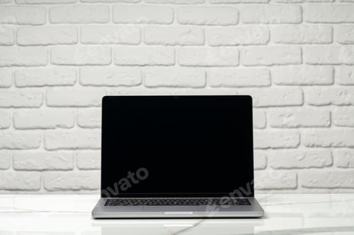 Preview: Laptop with black screen on desk against white brick wall