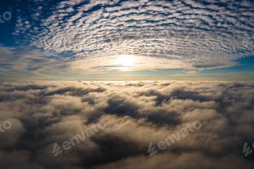 Preview: Aerial view of vibrant yellow sunrise over white dense clouds with blue sky overhead.