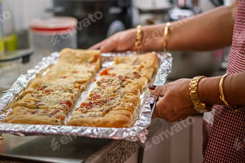 Preview: Woman holding baking tray with sliced garlic bread covered in cheese and herbs