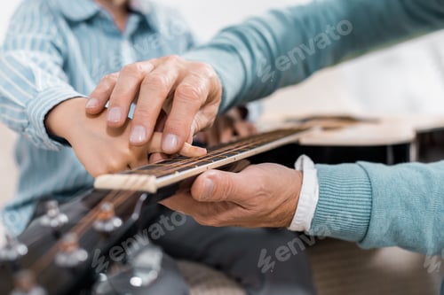 Preview: cropped image of man teaching child playing on acoustic guitar at home