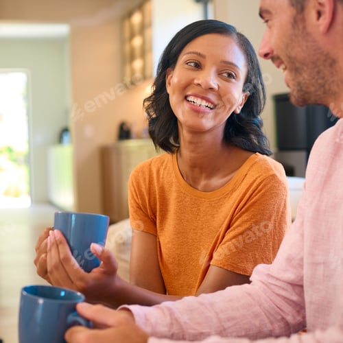 Preview: Loving Multi-Racial Couple Sitting On Sofa At Home With Hot Drink Laughing And Talking