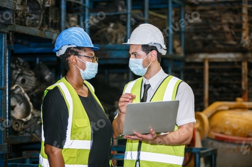 Preview: Team engineering two nationality wear face mask uniform working with computer laptop at factory.