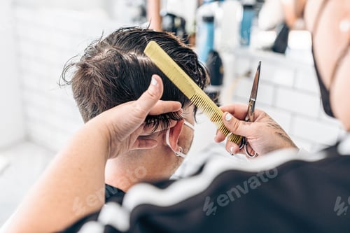Preview: Hairdresser using a comb and scissors to cut the hair of a young man in a salon