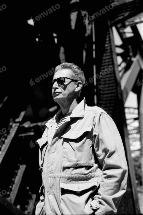 Preview: Senior engineer wearing sunglasses posing under metal structure in monochrome analog film style