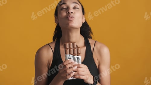 Preview: Young Afro woman dressed in sport bra holding chocolate bar send