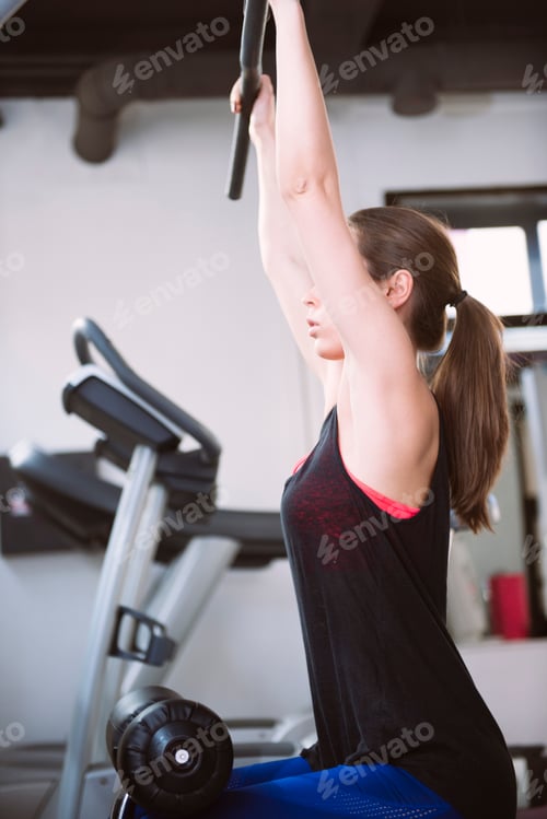 Preview: Attractive young woman working out on weight lifting training machine