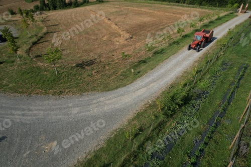 Preview: Farmer driving red tractor on gravel road next to farmland