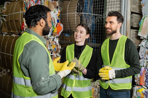 Preview: Indian worker in high visibility vest and gloves talking to smiling colleagues while standing
