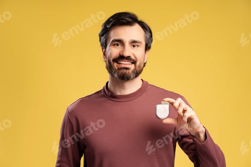 Preview: Portrait of attractive man holding pacemaker in hand, isolated in yellow background